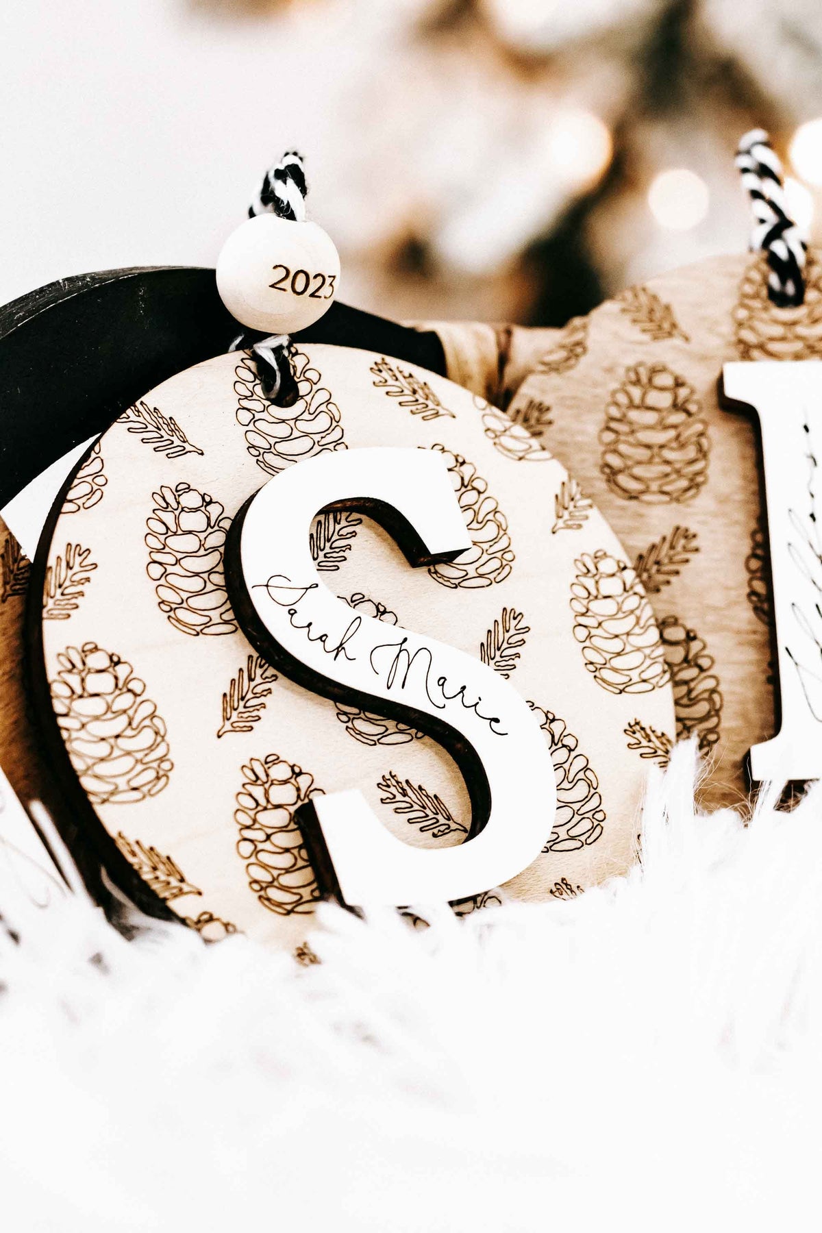 Round engraved pine cone ornament with letter S, zebra-striped cord and year 2023 tag