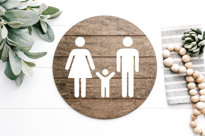 Round wood restroom sign with raised female, male, and child icons