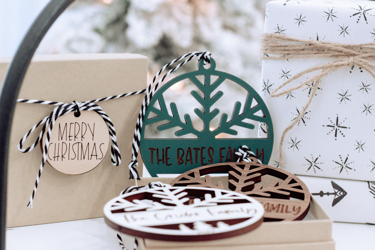 Round engraved ornament with family name and tree cutout, next to gift box and wrapped bundle