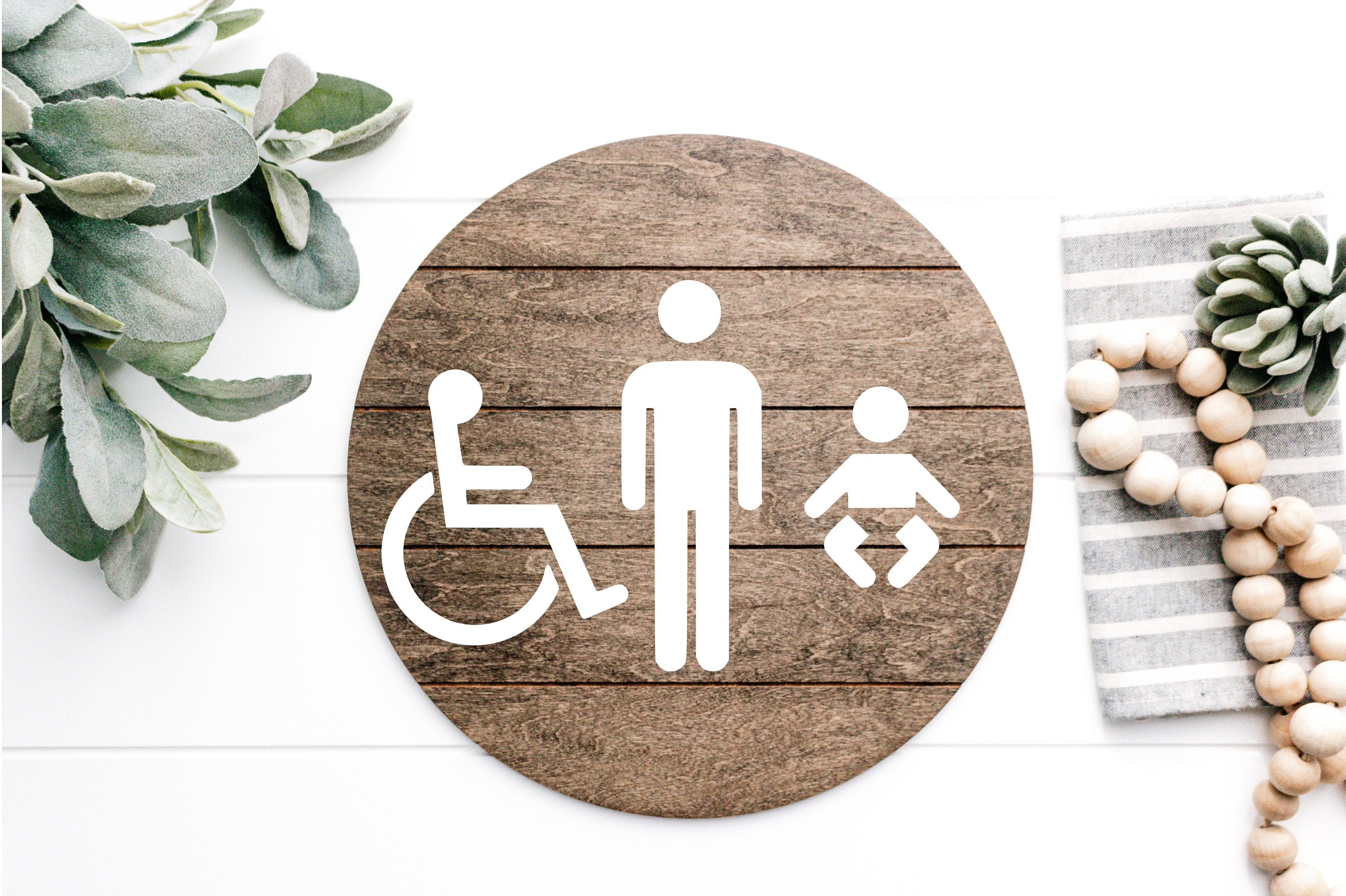 Round wood accessibility sign with male, wheelchair, and changing icons