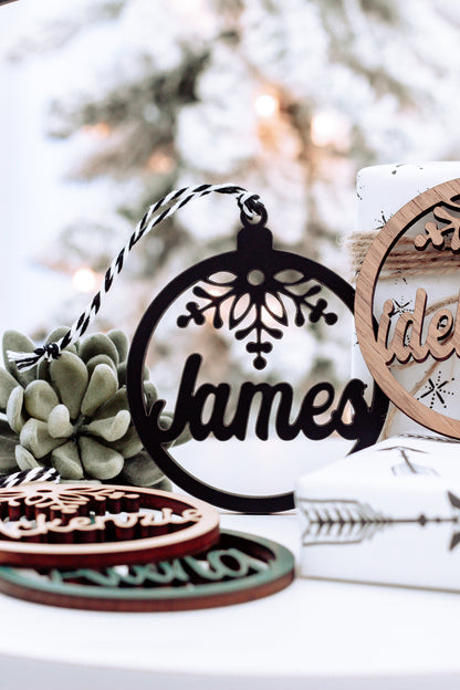 Round wooden name ornament with snowflake cutout and dark lettering, on a holiday set