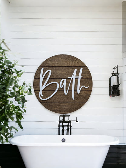 Round wooden bath wall sign with white “Bath” lettering above a bathtub