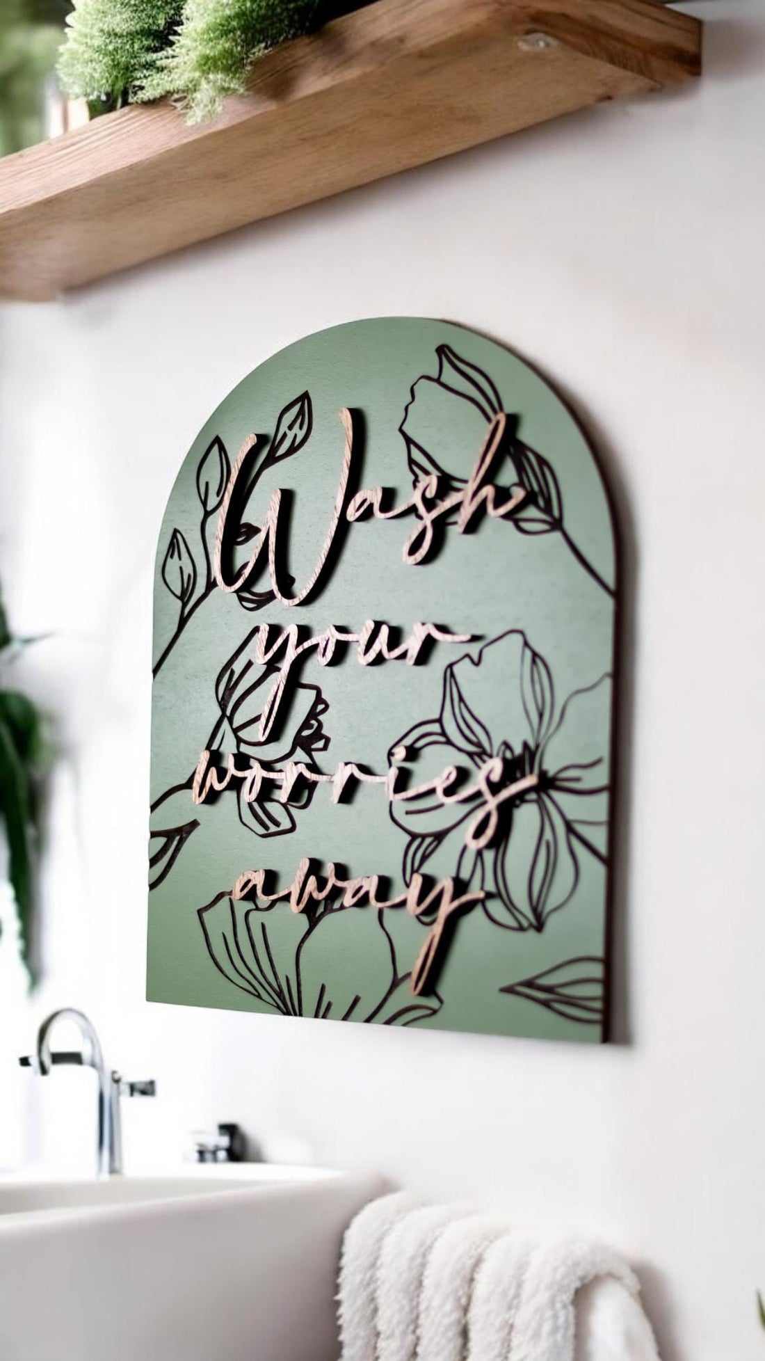 Floral engraved arch wall sign in muted green with dark “Wash your worries away” wording