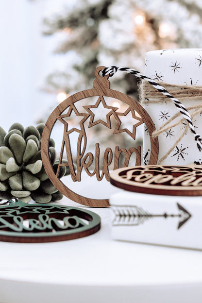 Brown wooden round name ornament with star cutouts and engraved name, tied gift