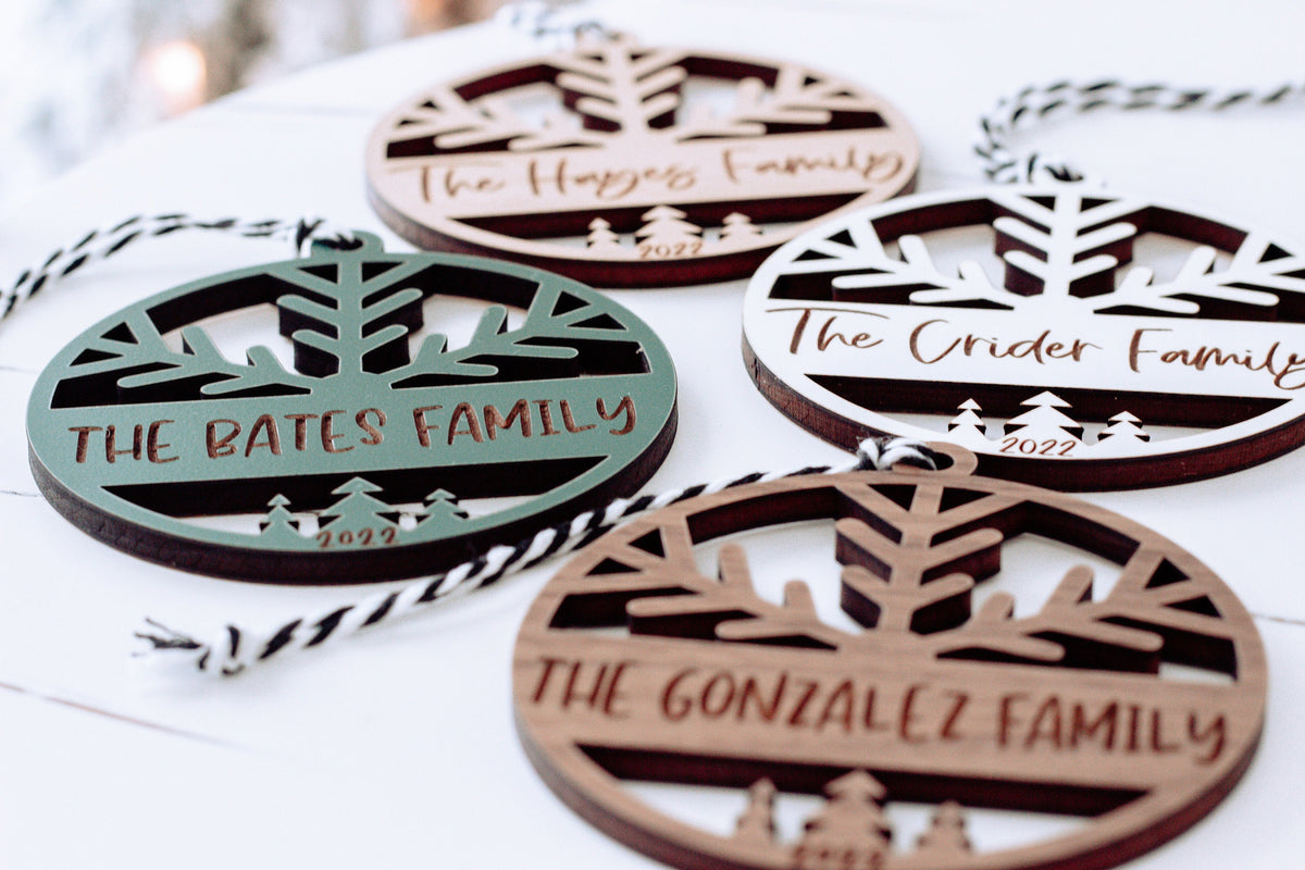 Engraved round ornaments with family names and tree cutouts in white, green, and dark wood
