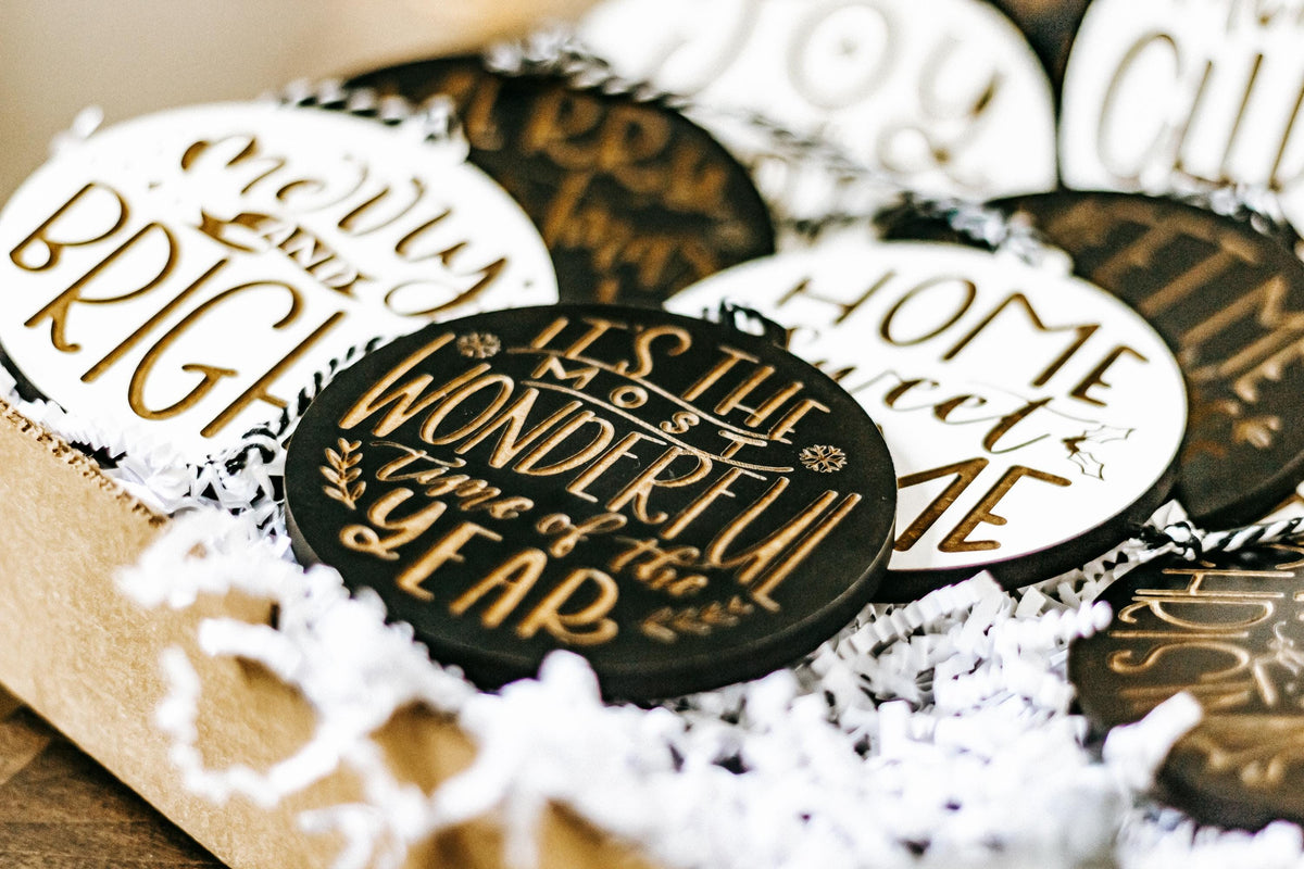Engraved Christmas ornaments, black and white hearts with gold text, nestled in a box.