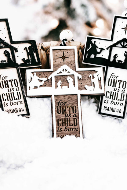 Group of dark and green nativity cross ornaments showing “for unto us a child is born”