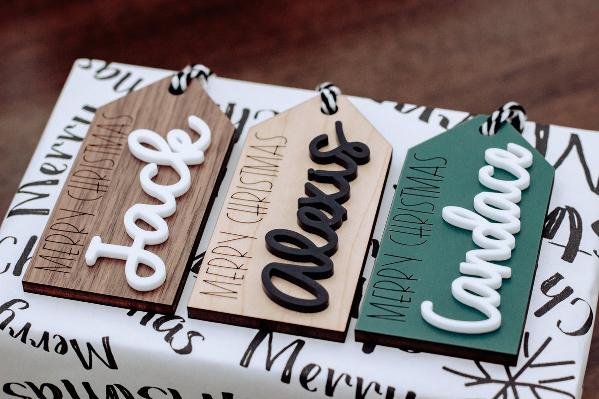 Wood gift tags laid out with Merry Christmas lettering in white, black, and green tones