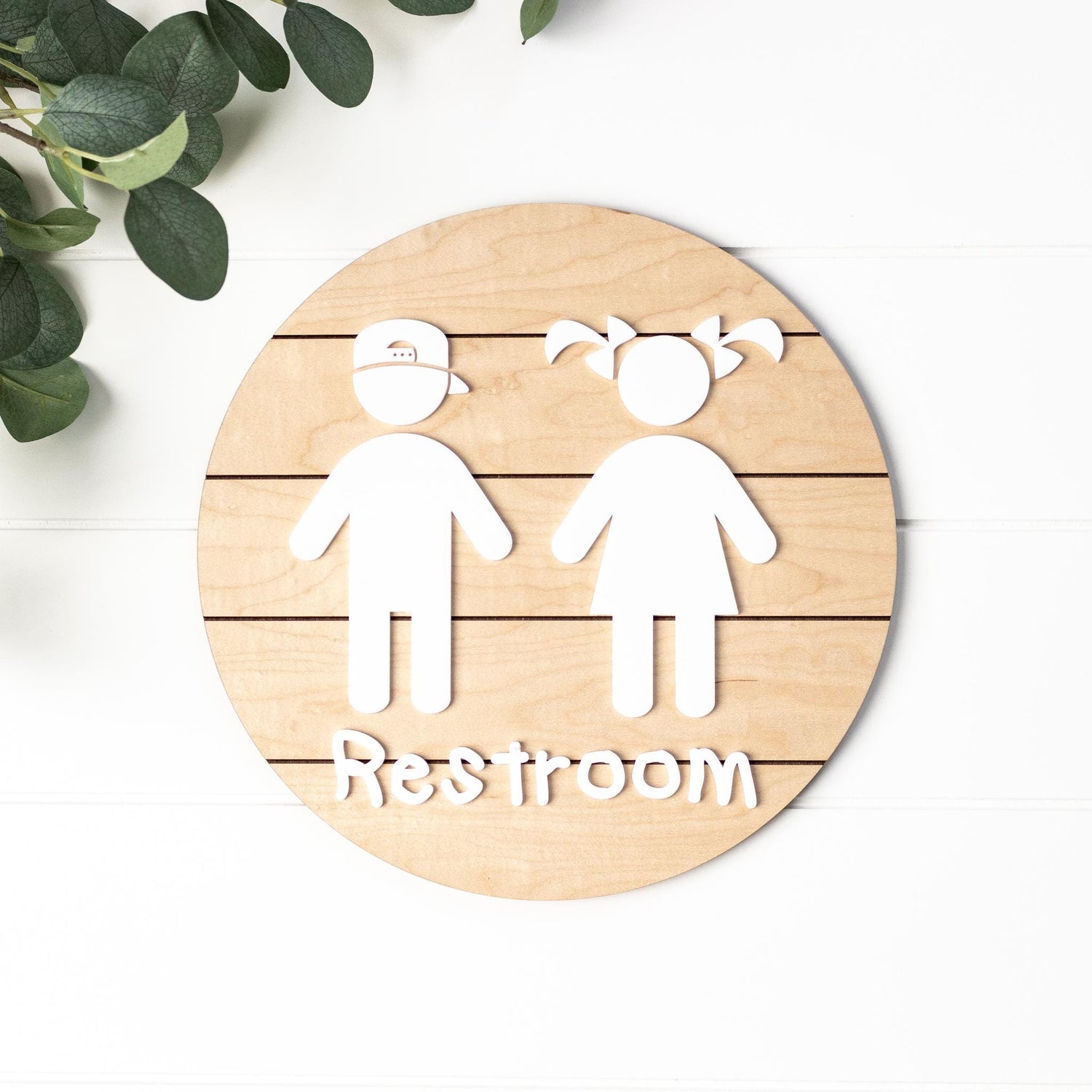 Round 3D toddler restroom sign in light wood with two white child figures and “Restroom”