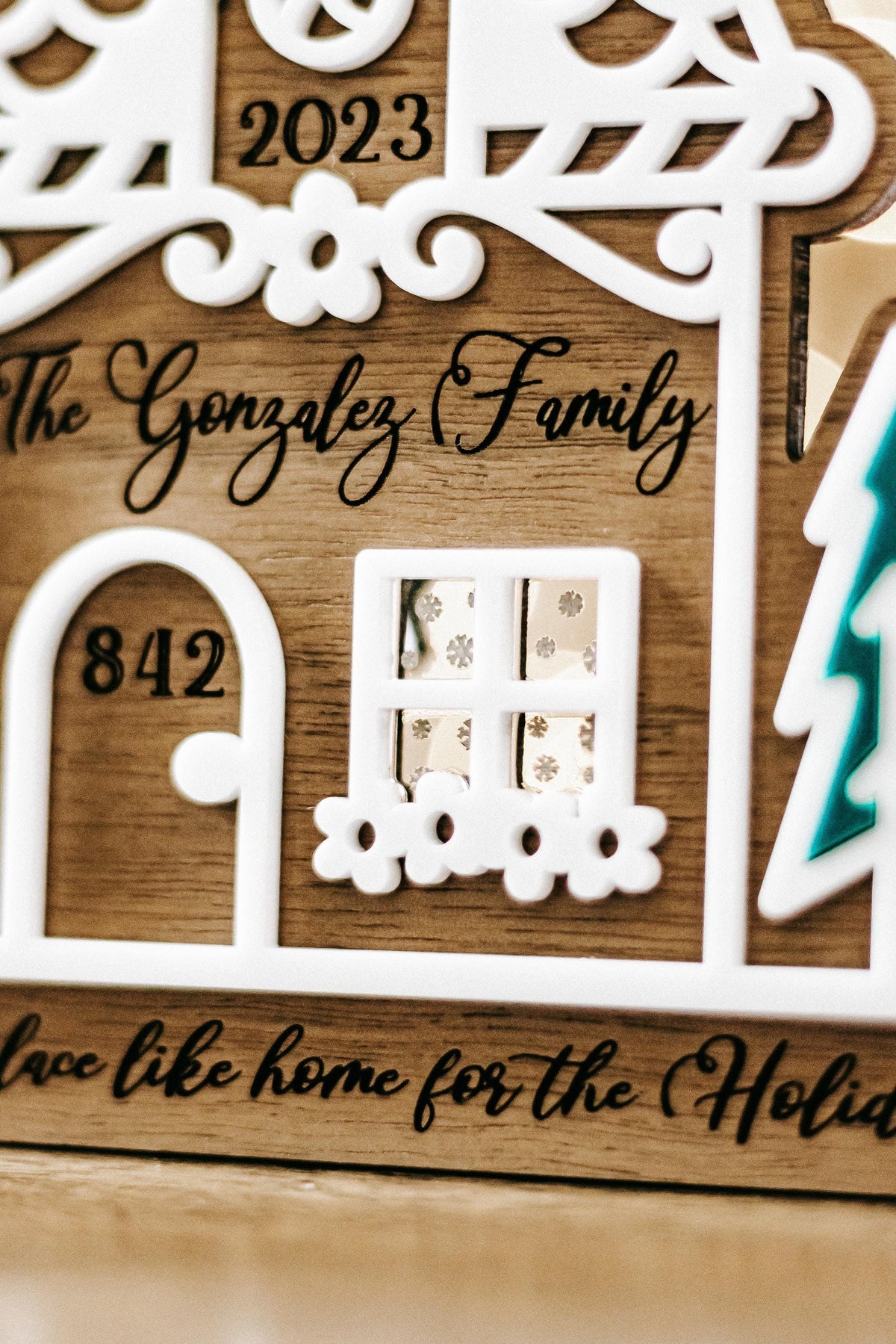 Wood gingerbread house ornament front with door “842,” window, teal tree, and holiday text