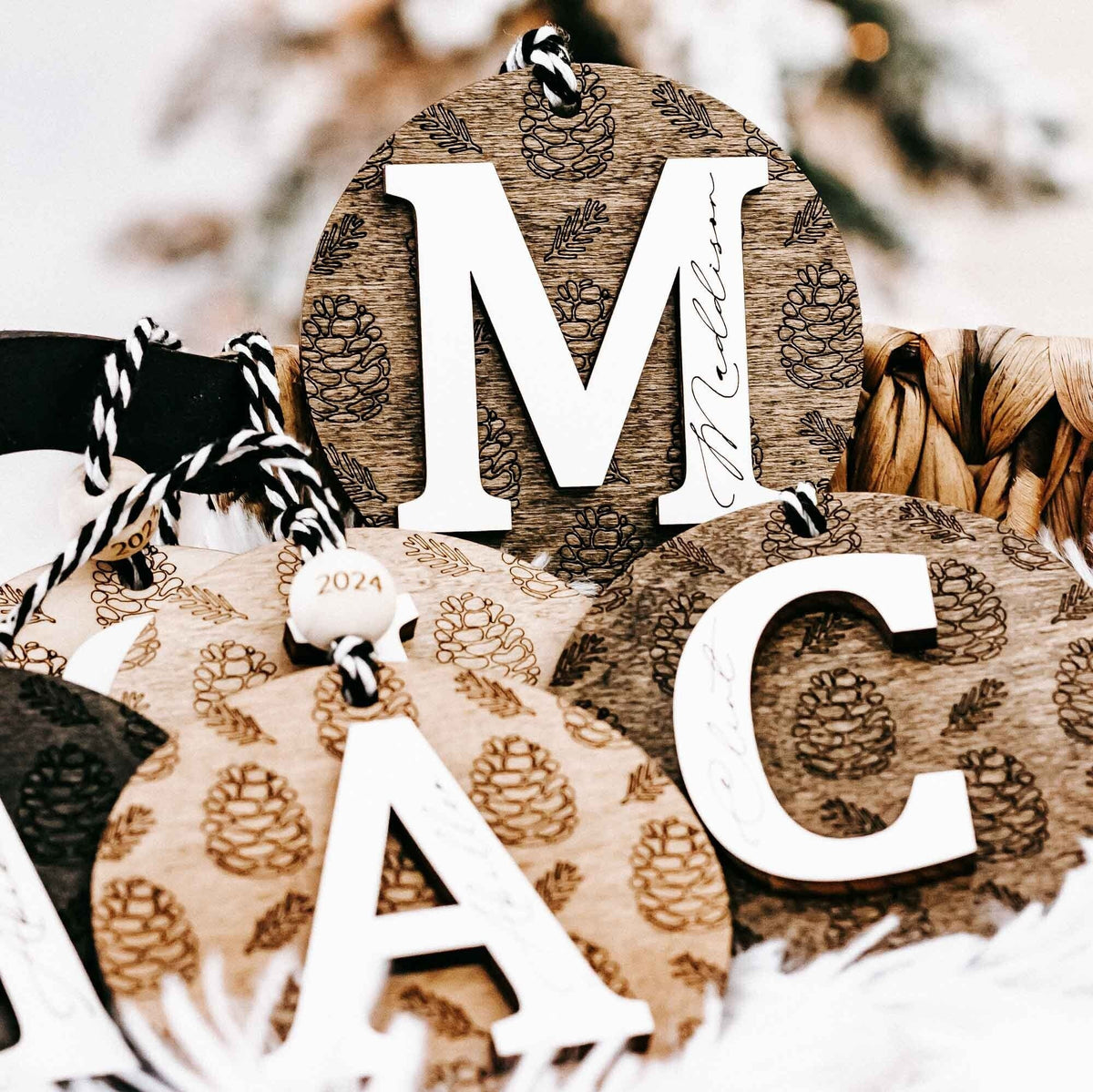 Round engraved pine cone ornament on black-and-white striped loop, year 2024