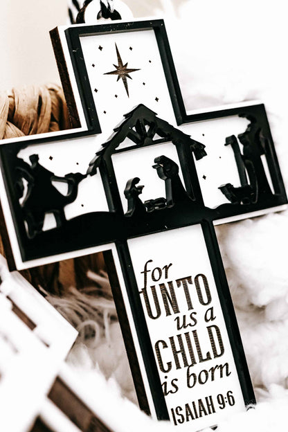 Black nativity cross ornament featuring manger scene silhouettes and “for unto us a child is born”