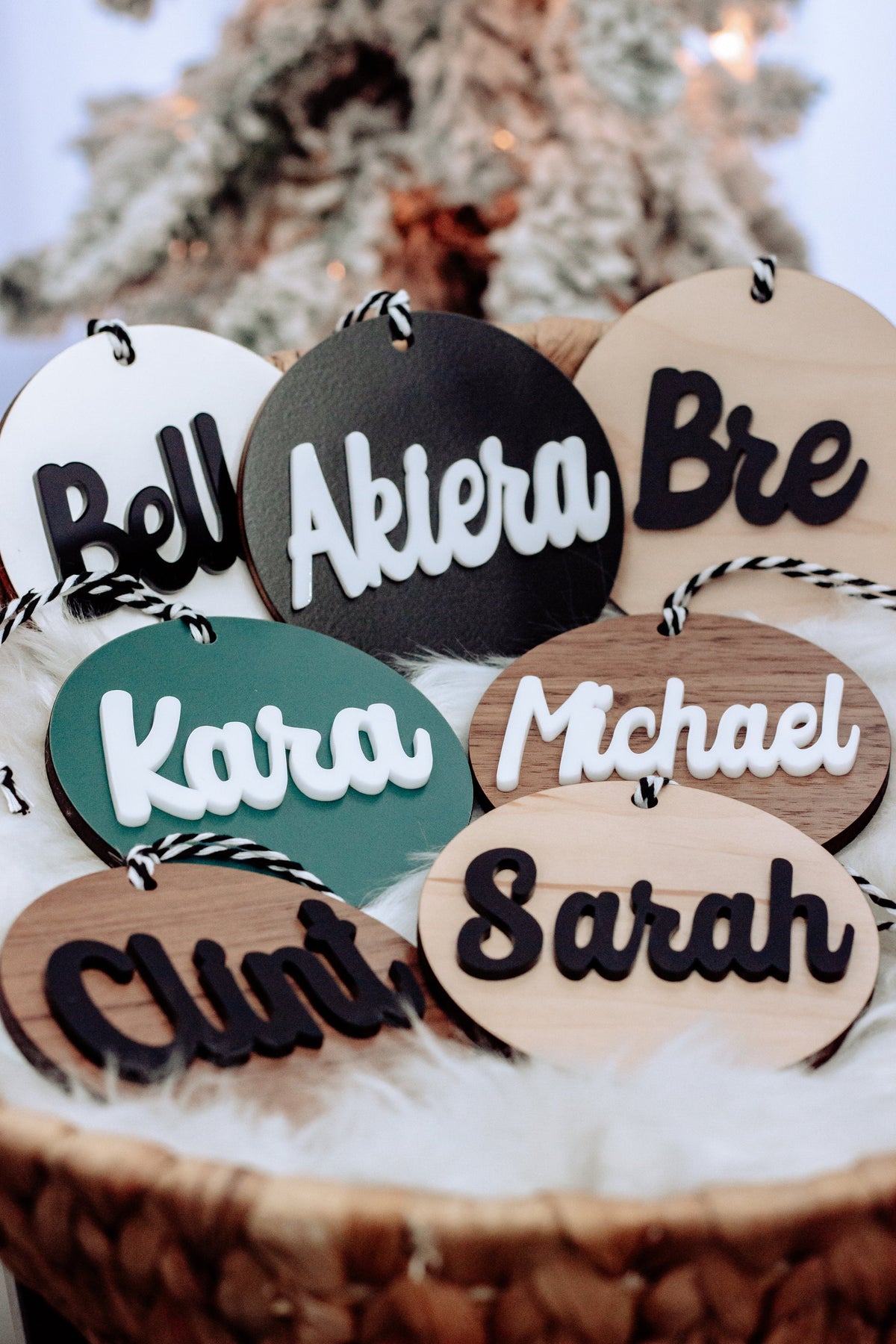 Round wooden name ornaments with rope hangers in white, charcoal, and tan with colored text