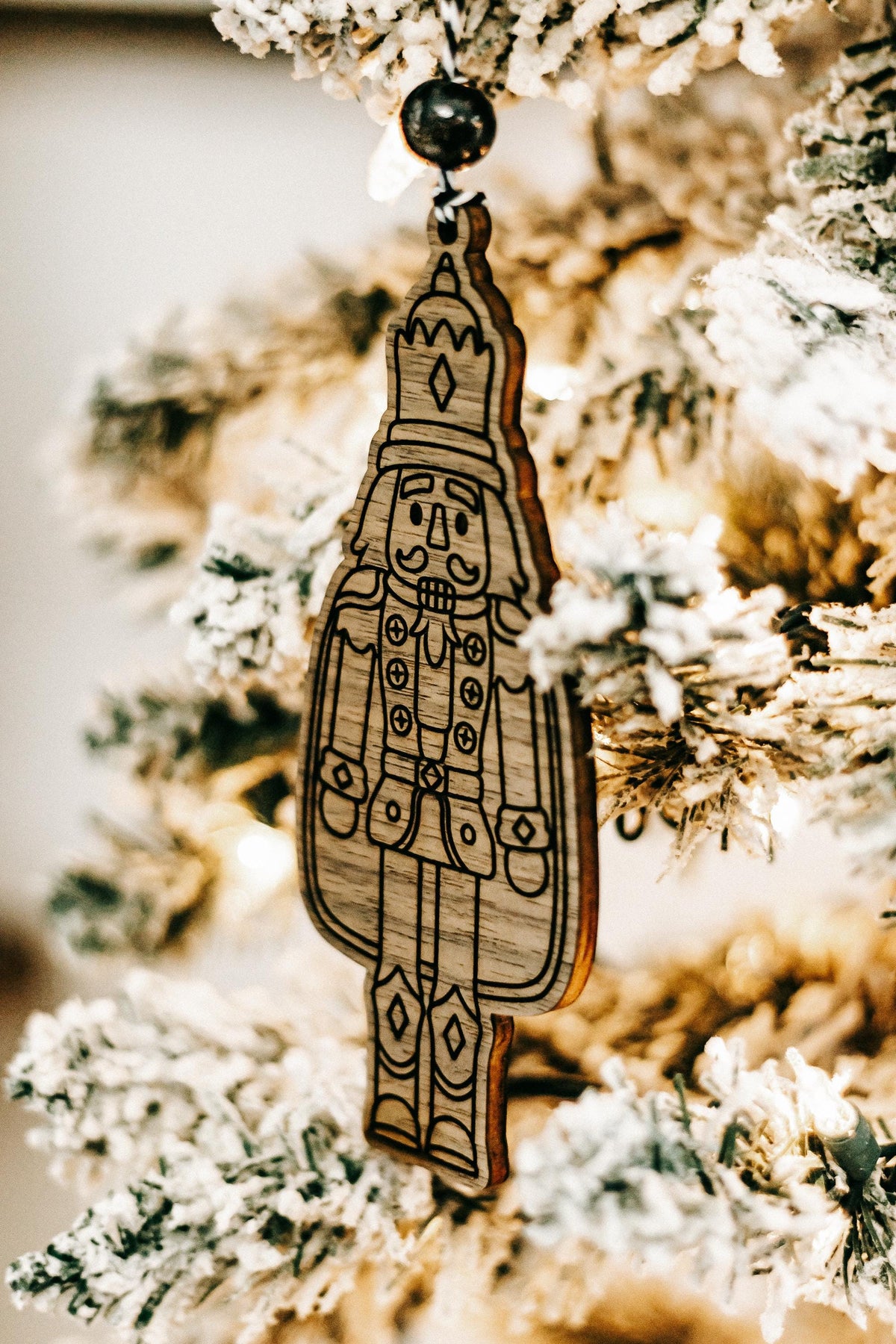 Engraved wooden nutcracker ornament hanging from a dark bead cord on a pine branch