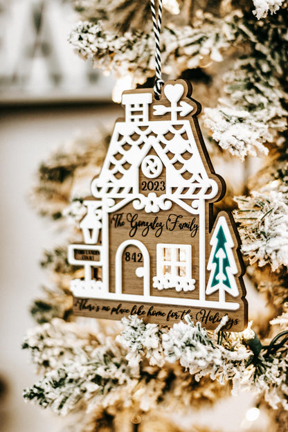 Wood gingerbread house ornament hanging on snowy branches with “2023” and teal tree