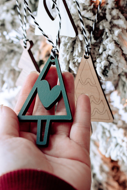 Hand holding a wooden Christmas tree ornament with striped string; green with heart cutout