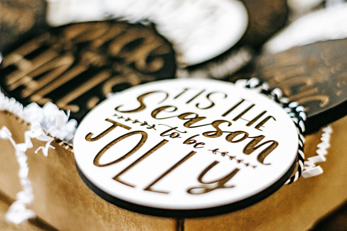 Close-up of engraved Christmas ornament text on a white circle with gold lettering, in box.