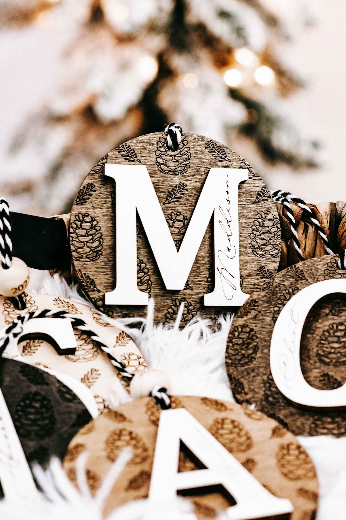 Round engraved pine cone ornament with letter M, zebra-striped hanging cord, year 2024