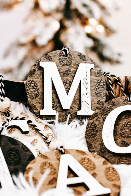Round engraved pine cone ornament with letter M, zebra-striped hanging cord, year 2024