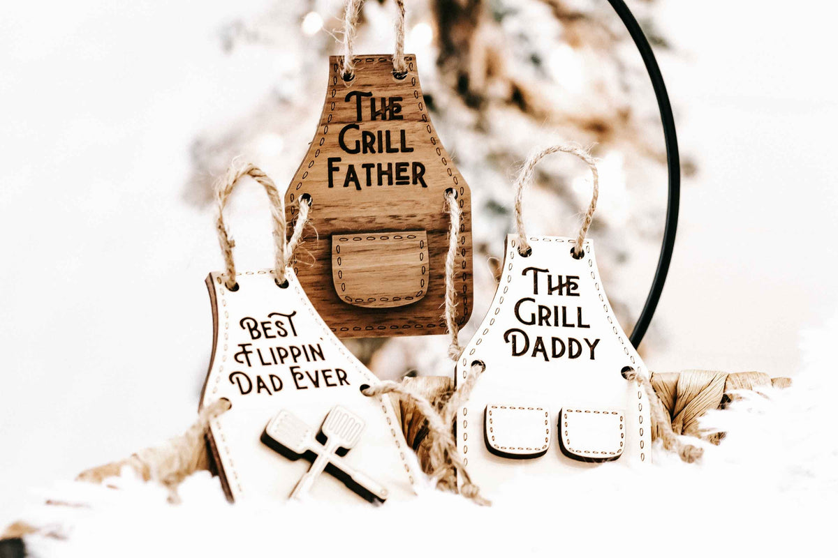 Wooden grill-themed holiday ornaments: “The Grill Father,” “Best Flippin’ Dad Ever,” and “The Grill Daddy.”