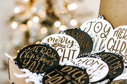 Engraved Christmas ornaments in a box, black and white round designs with gold lettering.