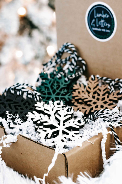 Snowflake Christmas ornament set with black, white, teal, and tan designs in a kraft box