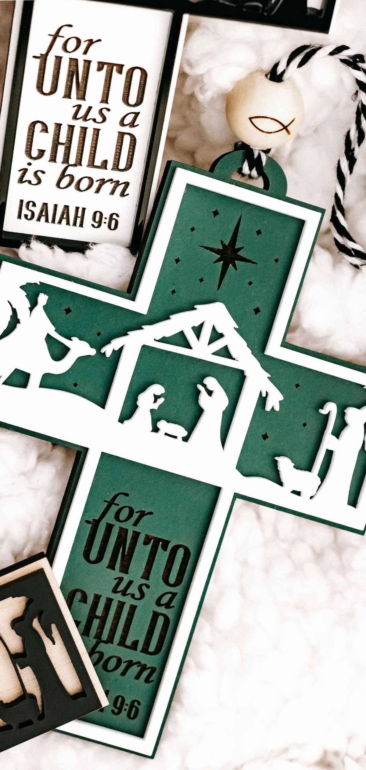 Close-up of green nativity cross ornament with verse text “for unto us a child is born”