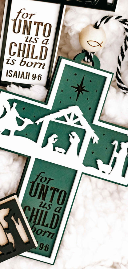 Close-up of green nativity cross ornament with verse text “for unto us a child is born”