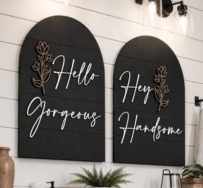 Two black arched wall signs with gold leaf details and white cursive text: Hello Gorgeous, Hey Handsome