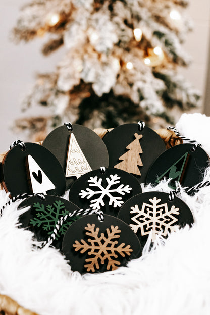 Black wooden ornament discs with snowflakes and a tan Christmas tree, hanging loops