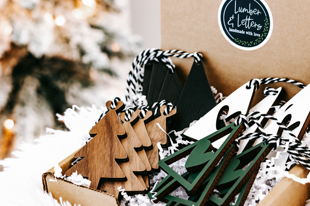 Stacked Christmas tree ornaments in kraft tray, wood and green with striped string hangers