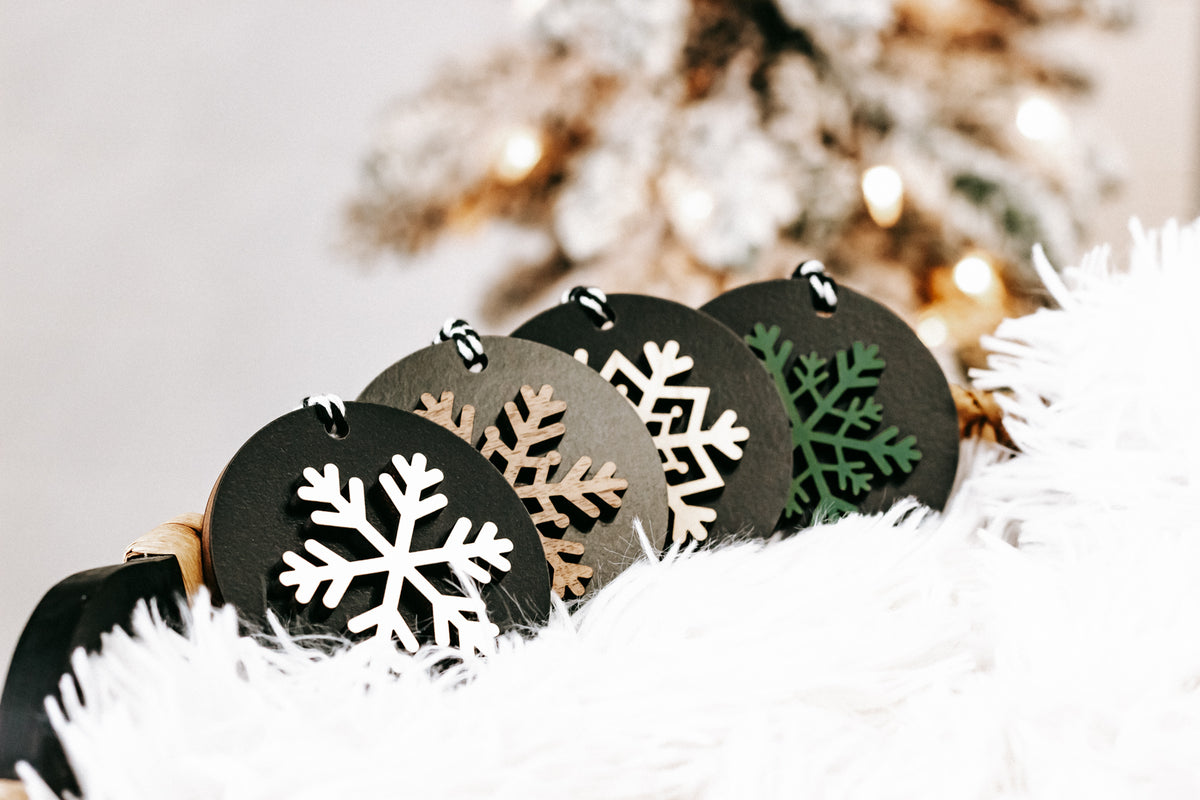 Black wooden ornament discs with white and multicolor snowflake cutouts, hanging loops