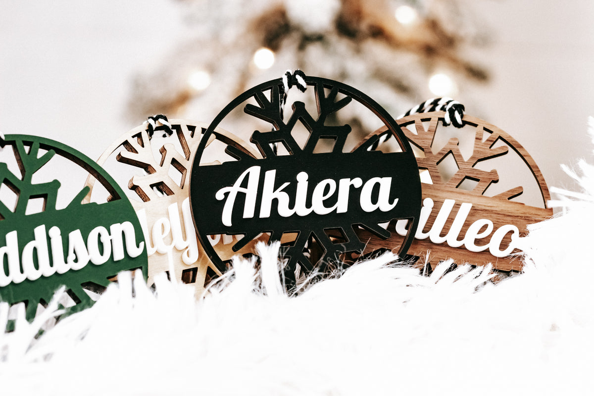 Wood snowflake ornaments with engraved names “Akiera” and “Akuleo” in a snowy display