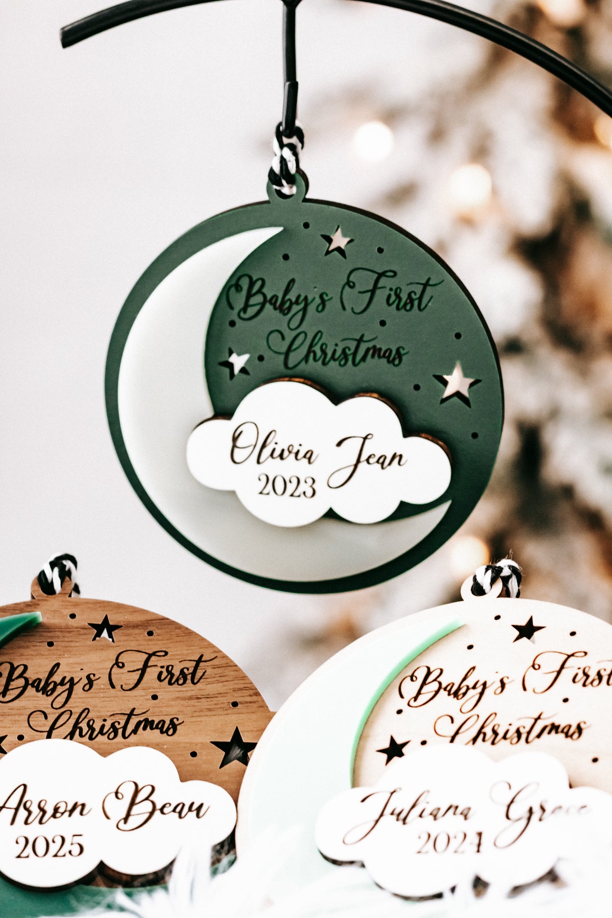 Green hanging round ornament with white cloud tag: Olivia Jean, 2023; other ornaments below.