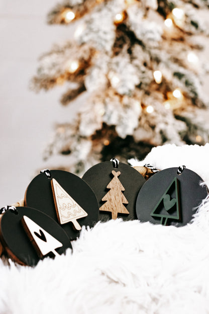 Black wooden ornament discs with white snowflakes and a tan tree, hanging loops