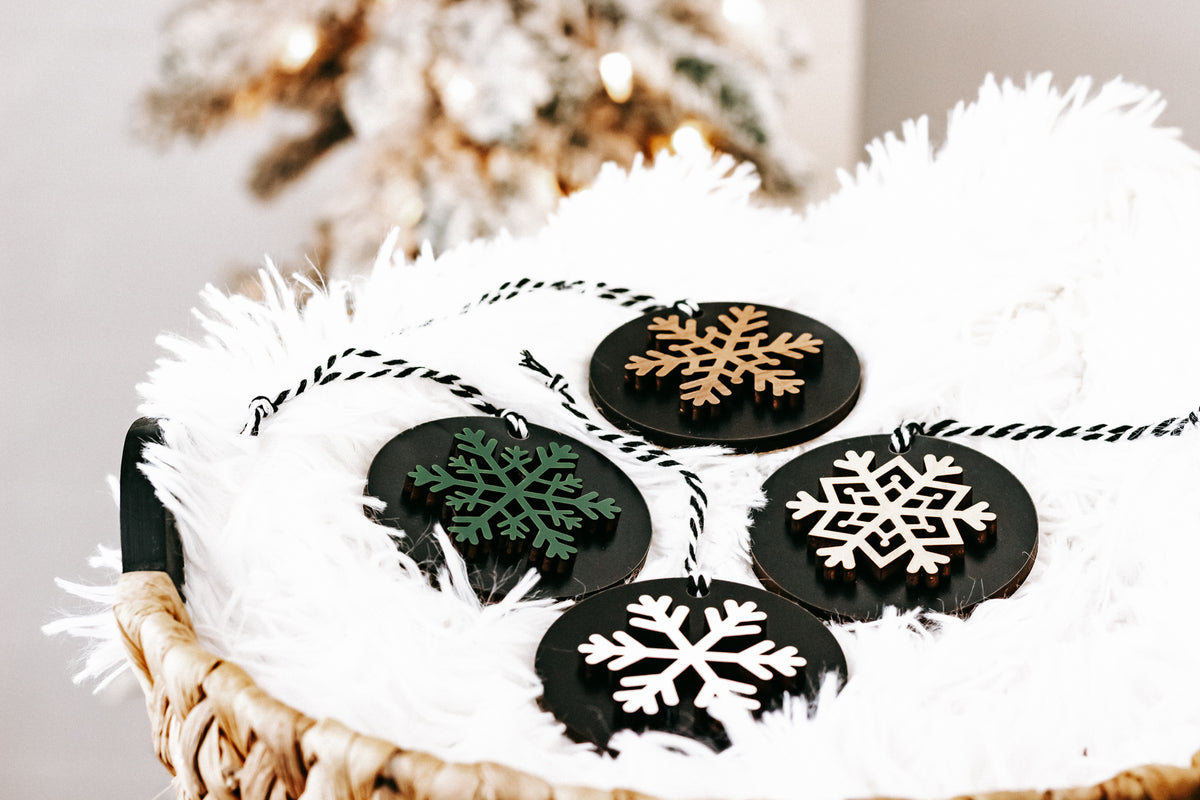 Black wooden ornament discs with mixed snowflakes in white, green, and tan, hanging loops