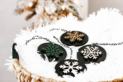 Black wooden ornament discs with mixed snowflakes in white, green, and tan, hanging loops