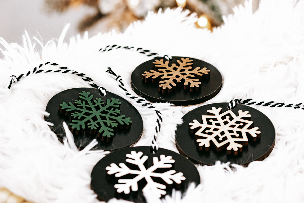 Black wooden ornament discs with white snowflakes and green/tan accents, hanging loops