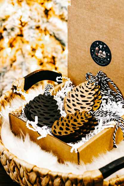 Hand-stained wooden pinecone ornaments: black and tan with hanging loops in tray
