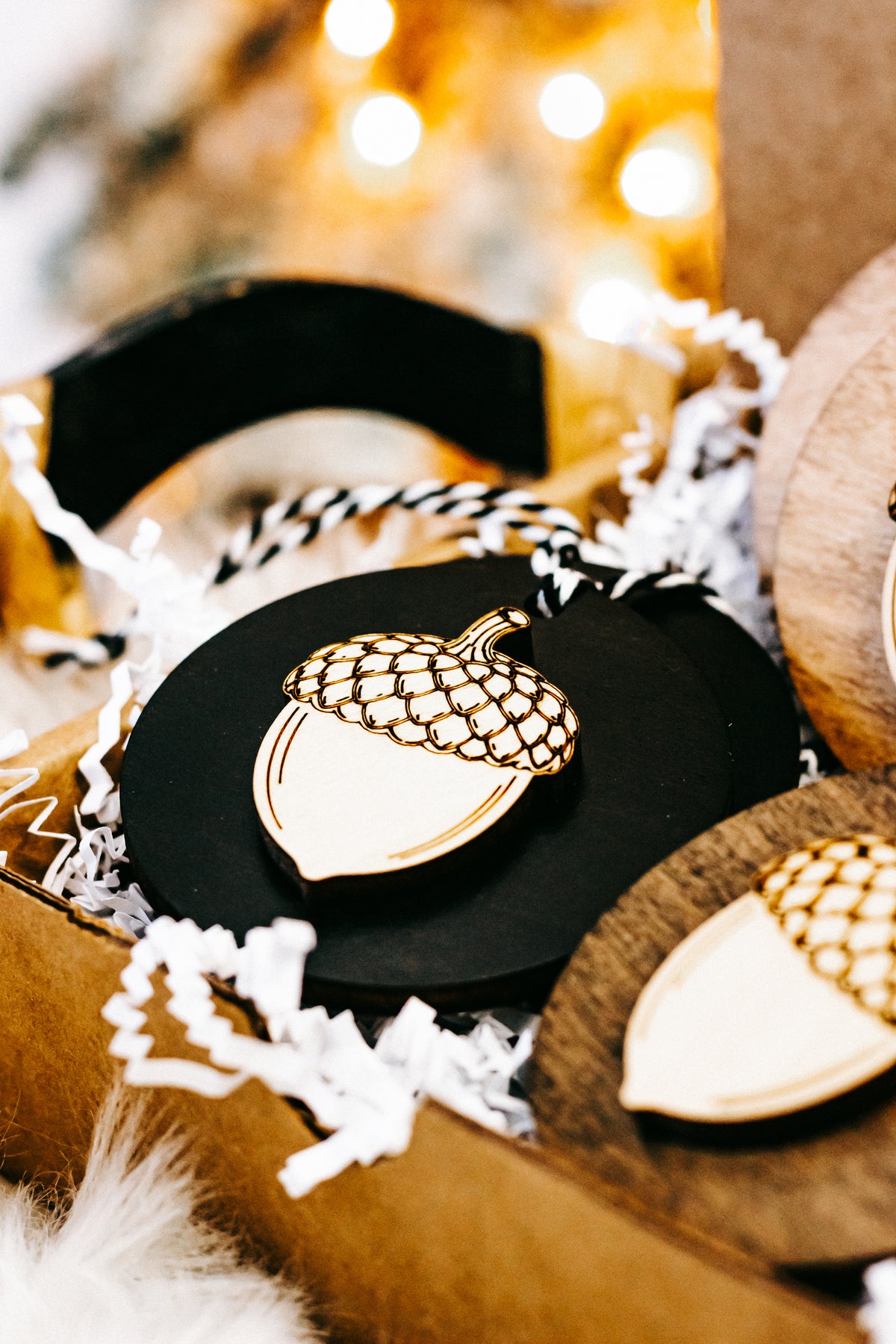 Close-up round acorn ornament: black disc with white acorn, gold checkered cap, twine loop.