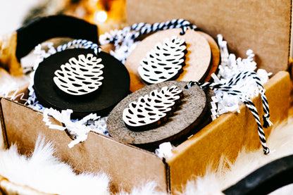 Wooden pinecone ornaments in box, mixed black and wood discs with white pinecone cutouts