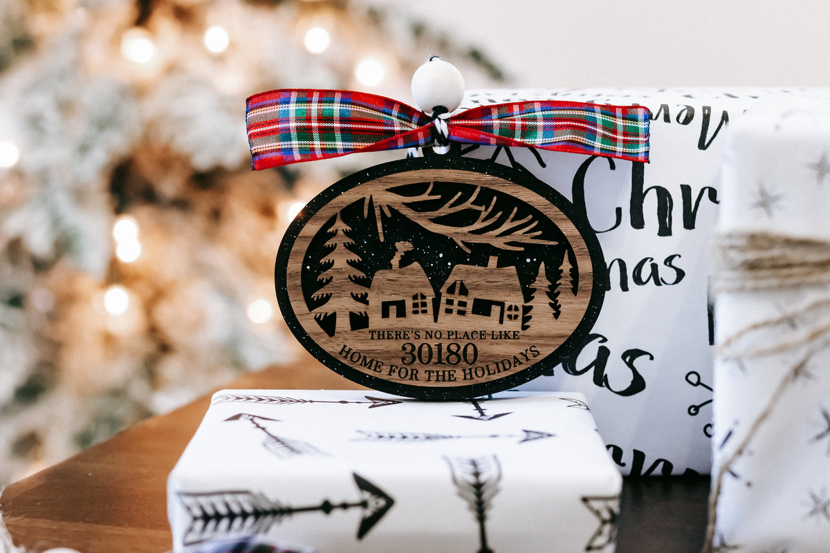 Round Christmas ornament with house scene, plaid bow, hanging loop; zip code 30180.