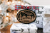 Round Christmas ornament with house scene, plaid bow, hanging loop; zip code 30180.