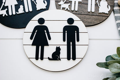Close-up of round restroom sign with pet silhouettes, white icons on black-and-tan