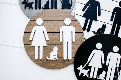 Round restroom sign with pet silhouettes, white icons on tan circle beside a black sign
